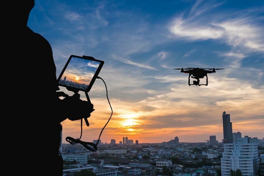 Man playing with the drone. Silhouette against the sunset sky over the city.